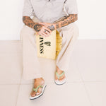 Man with tattoos wearing collared shirt, beige pants and white and green mens flip flops