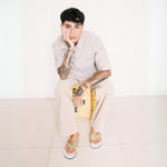 Man with tattoos wearing collared shirt, beige pants and white and green mens flip flops