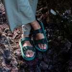 Woman's feet on volcanic rock wearing Green Adventure Sandals