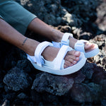 woman's feet wearing white adventure sandals against black volcanic rock