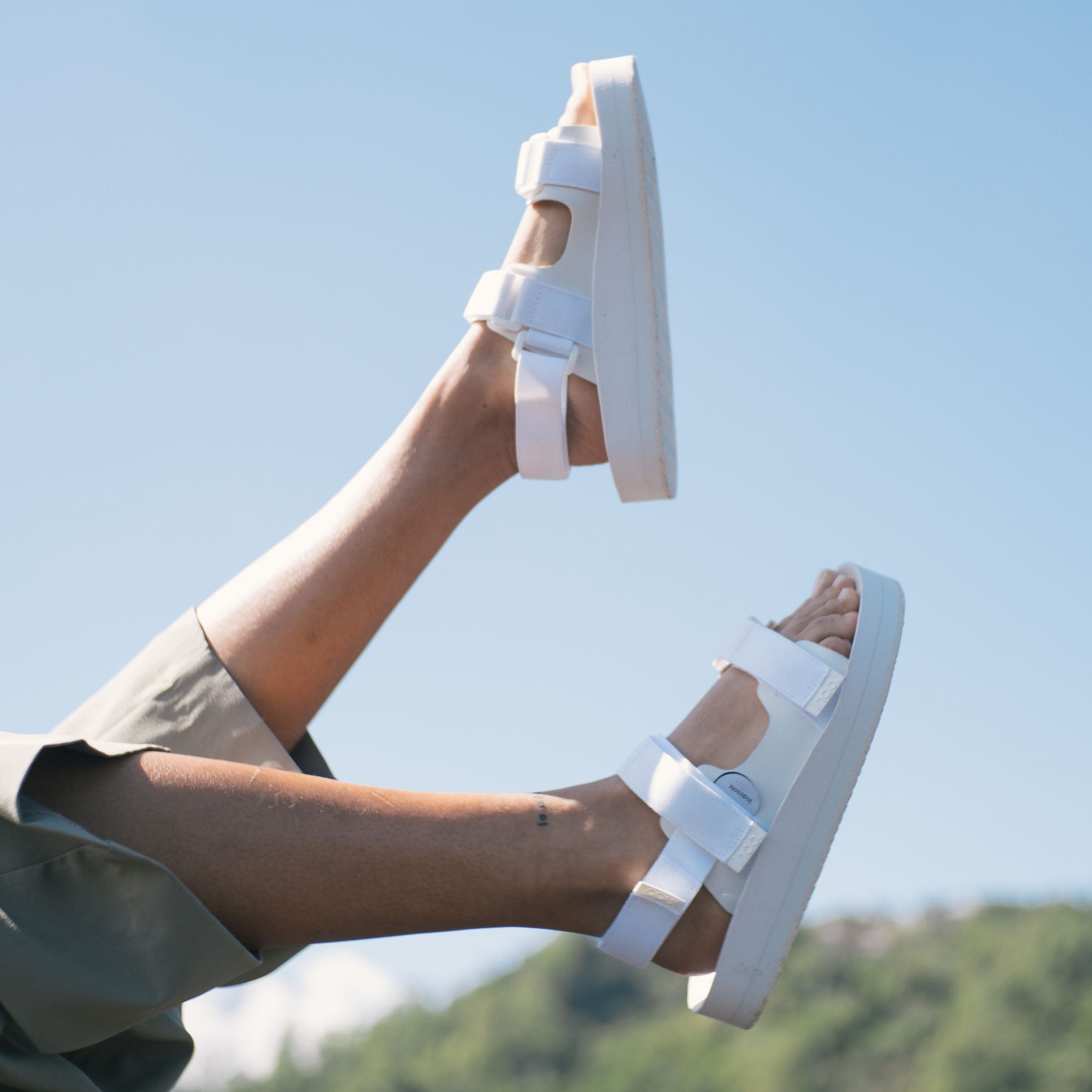 woman's feet in the air wearing white adventure sandals