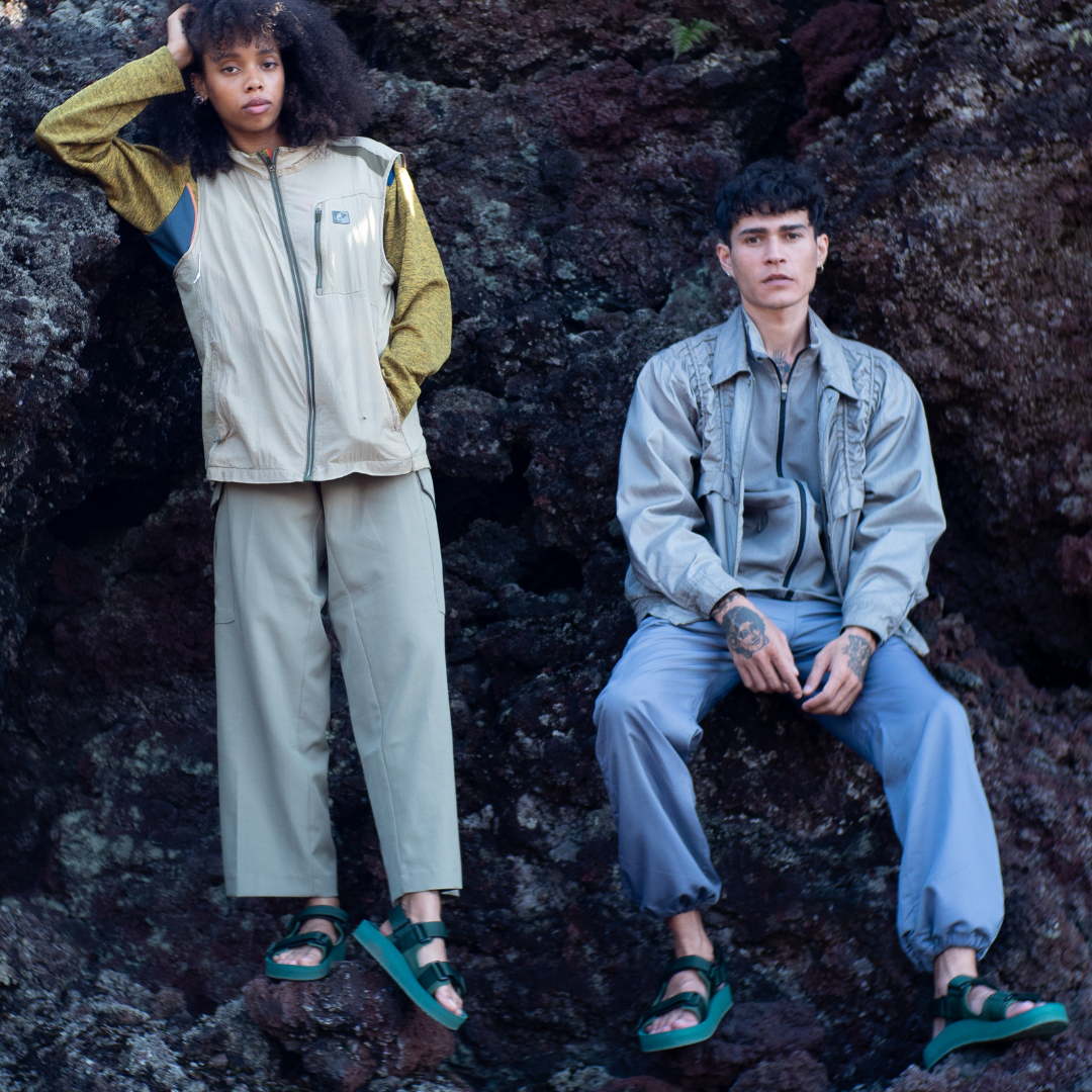 Two people - a man and a woman - standing on a rocky hillside wearing outdoor clothing and adventure sandals