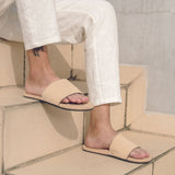 Man wearing light soil slides and white pants sitting on cream colored stairs
