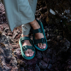 Woman's feet on volcanic rock wearing Green Adventure Sandals 