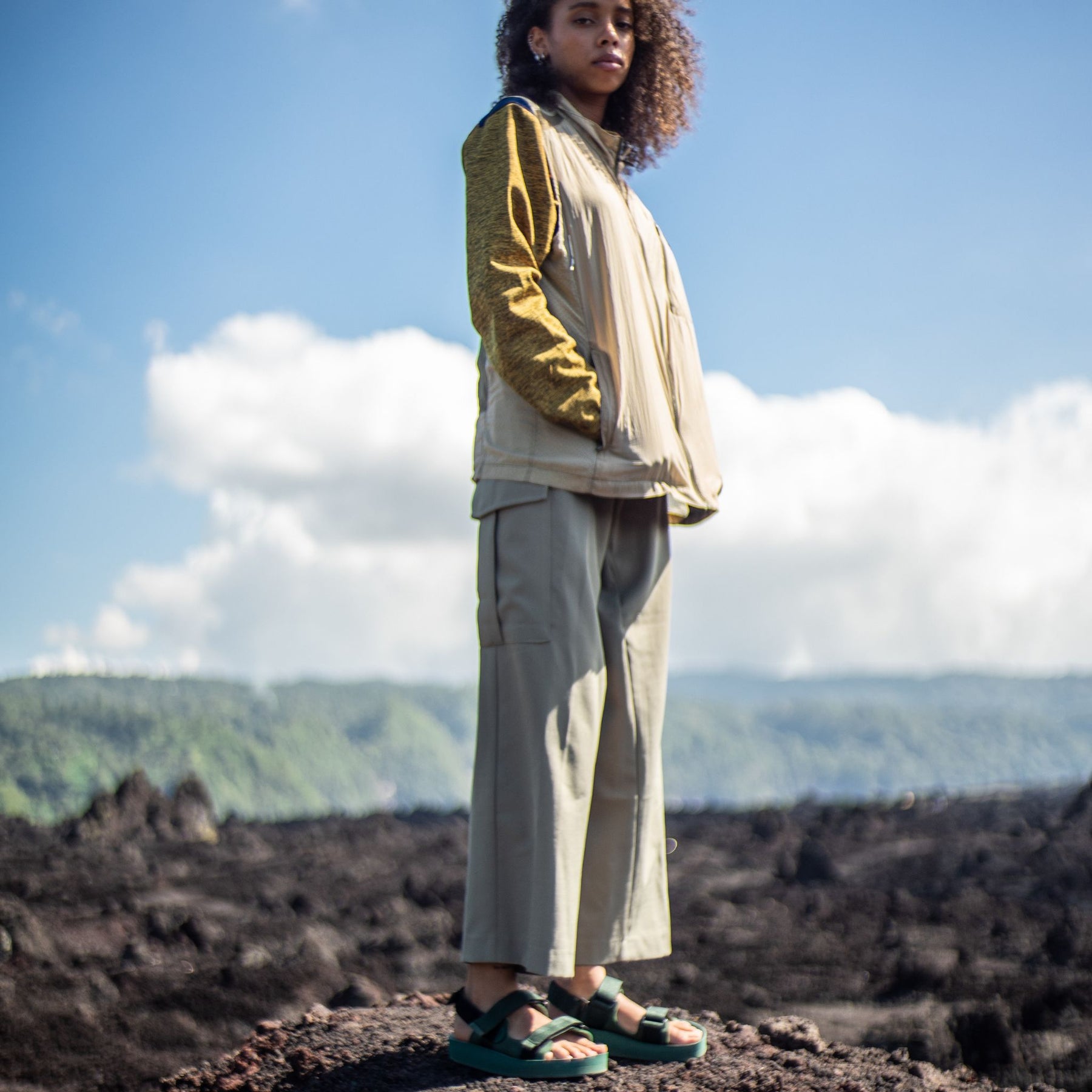 Woman standing on volcanic rock wearing Green Adventure Sandals 