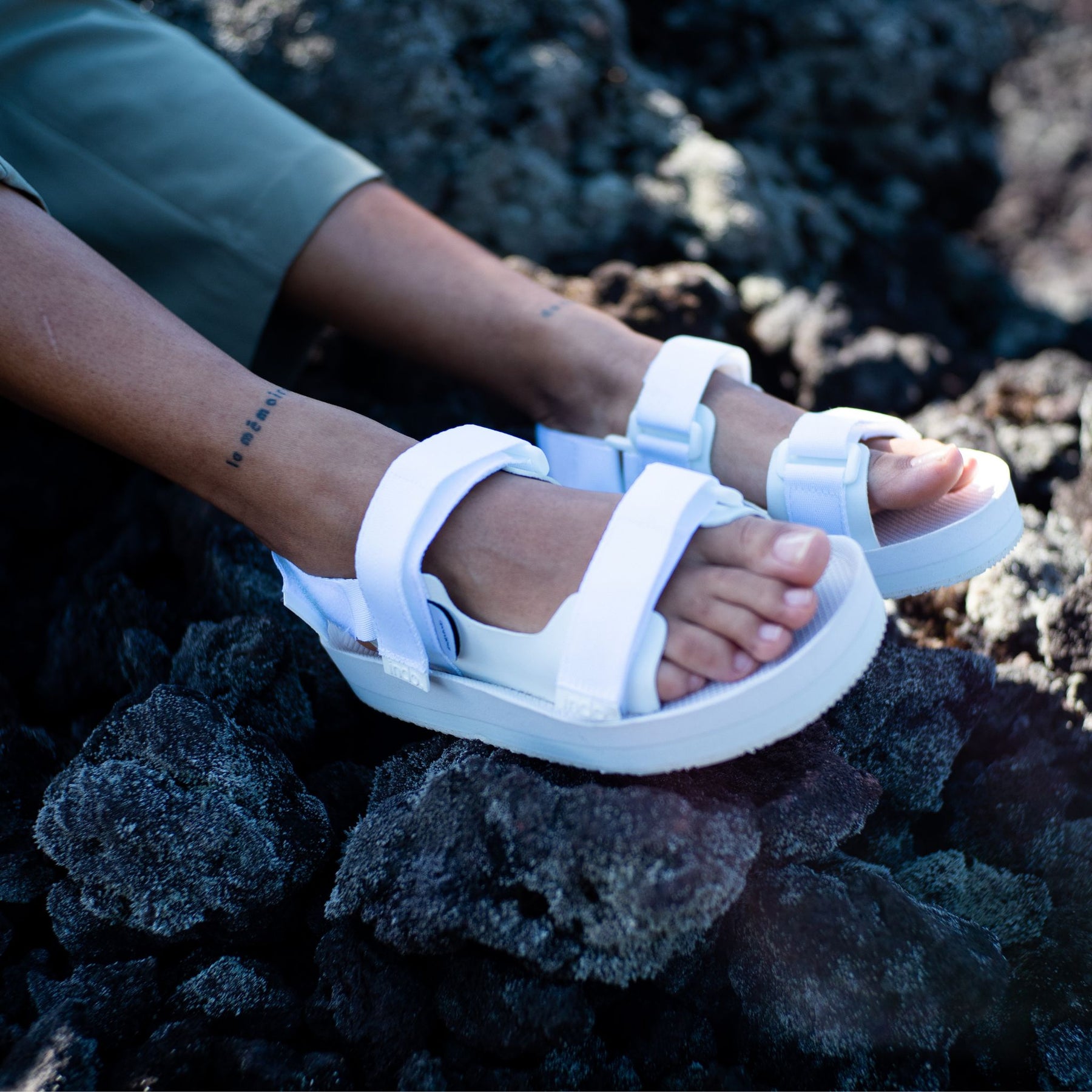 woman's feet wearing white adventure sandals against black volcanic rock