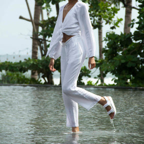 Woman wearing white linen clothing and white adventure sandals walking in shallow water