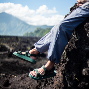 Man wearing green sandals sitting on rock outdoors