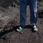 man standing on mountainside wearing green adventure sandals