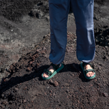 man standing on mountainside wearing green adventure sandals