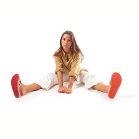 A woman sitting on the ground wearing Red Sole/Sea Salt Flip Flops