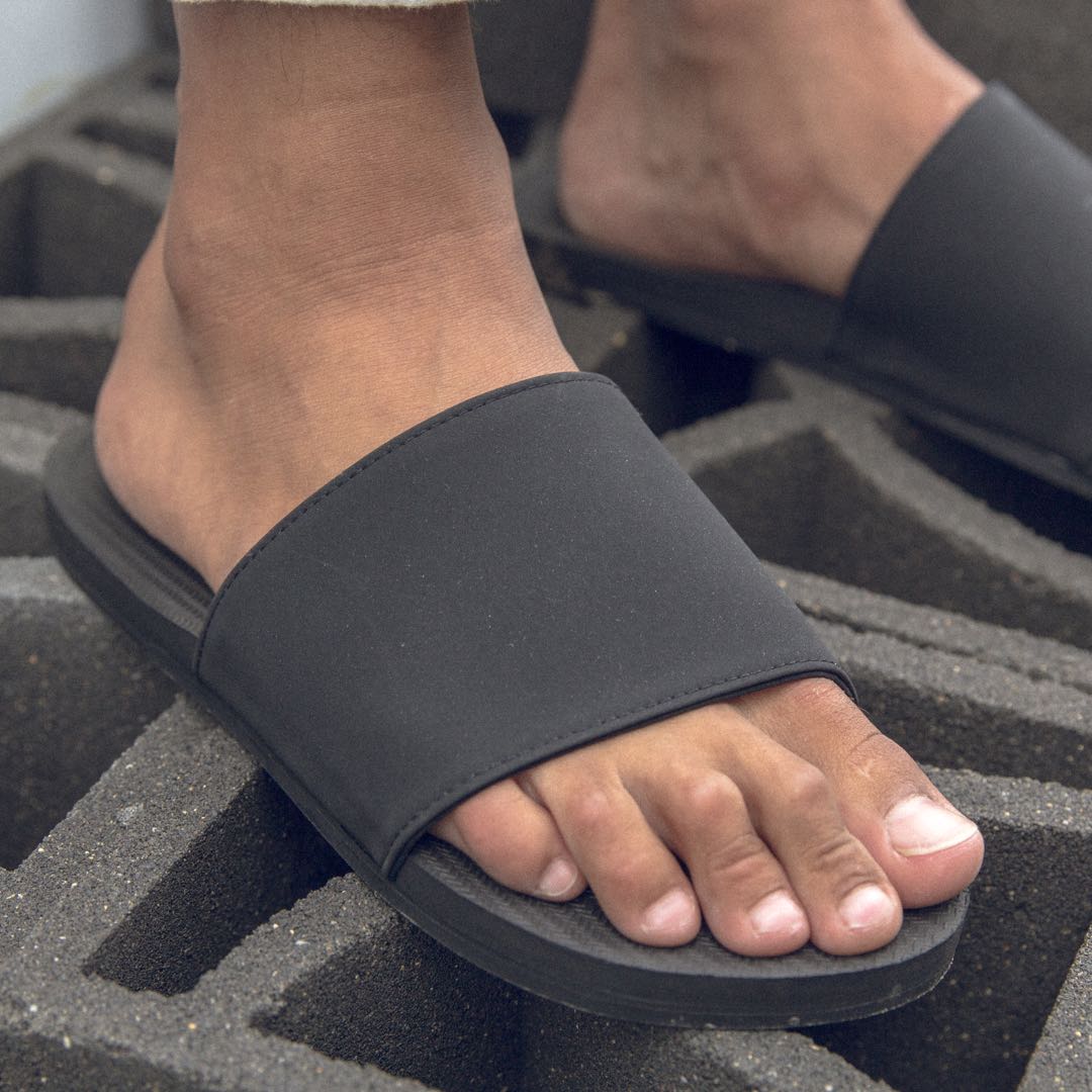 Man wearing black slides standing on cement bricks