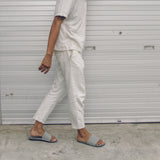 Man wearing grey slides and white trousers walking in urban street (2385873600589)