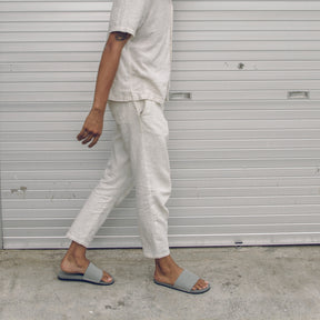 Man wearing grey slides and white trousers walking in urban street (2385873600589)