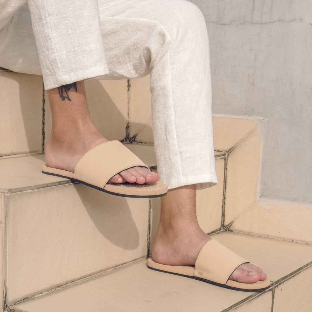 Man wearing light soil slides and white pants sitting on cream colored stairs