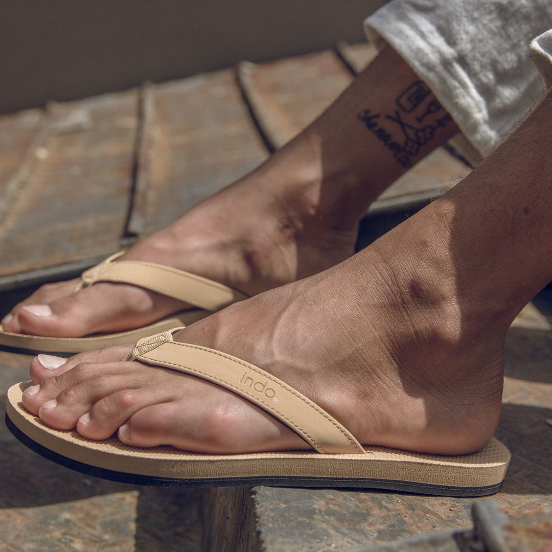 Man wearing light soil flip flops with an ankle tattoo