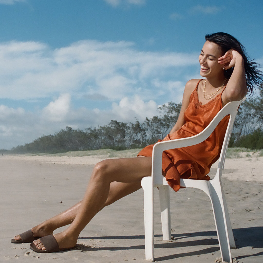 Woman sitting on beach wearing brown/soil slides