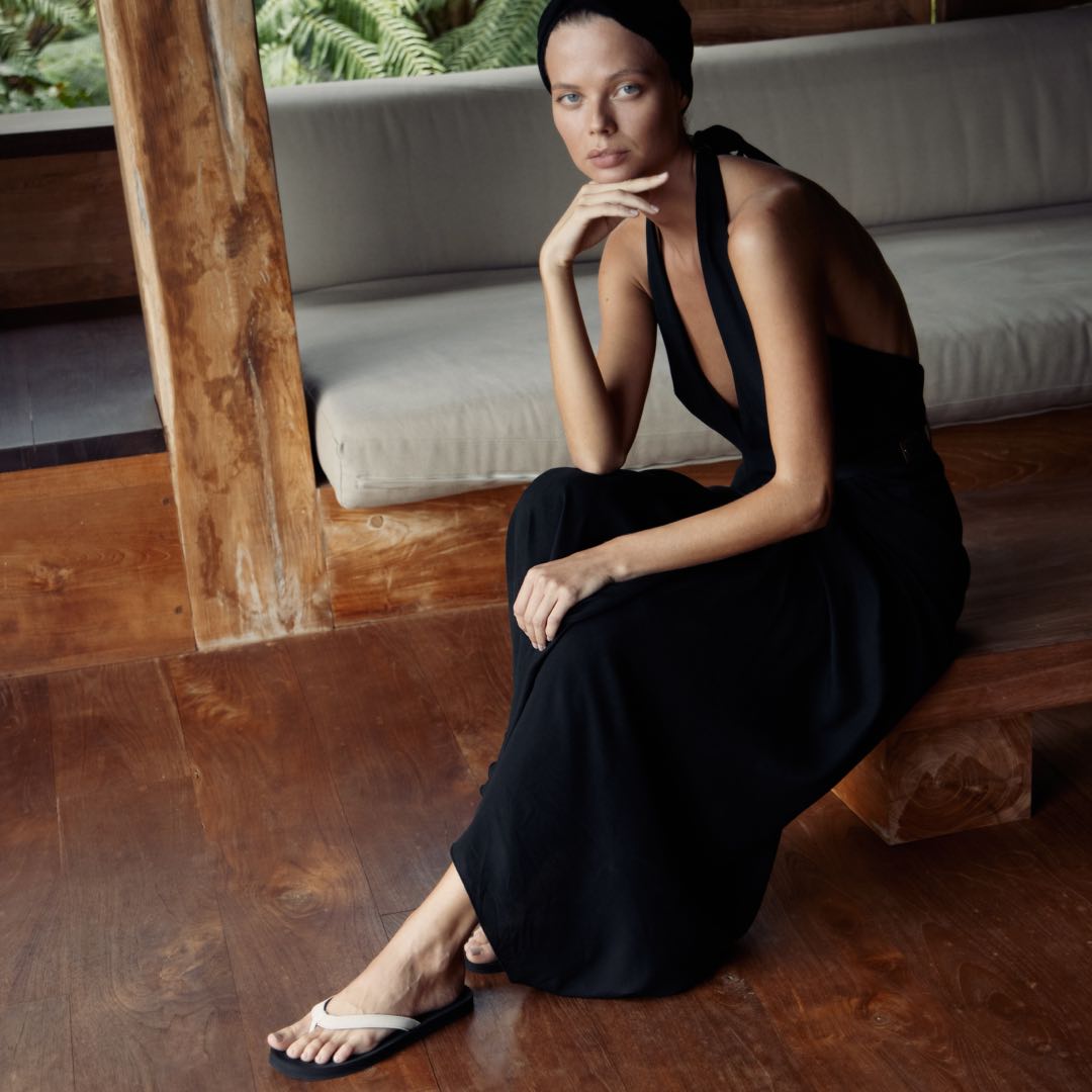 Woman sitting wearing black/sea salt flip flops