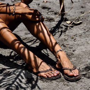 Woman wearing soil flip flops sitting on wet sand