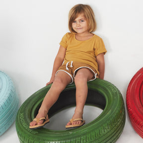 A toddler sitting wearing light soil flip flops